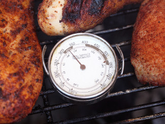 A grill with chicken and a thermometer.