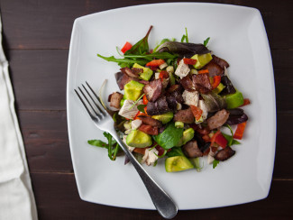 A plate of a salad with chicken, bacon, avocado, peppers, and greens.