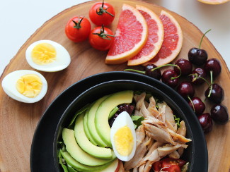 A tray with an assortment of Paleo-approved foods like cherries, tomatoes, grapefruit, chicken, and greens.