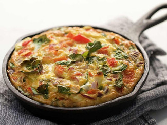 A Organic Mama Veggie Frittata in a cast-iron pan on top of a cloth napkin.